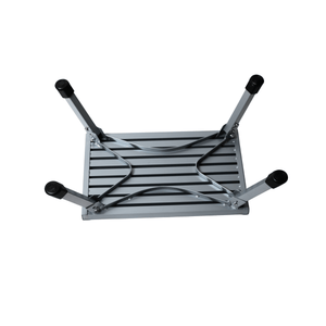 A silver aluminum folding table shown upside down, revealing its slatted metal base and four adjustable legs with black rubber end caps, isolated on a white background.