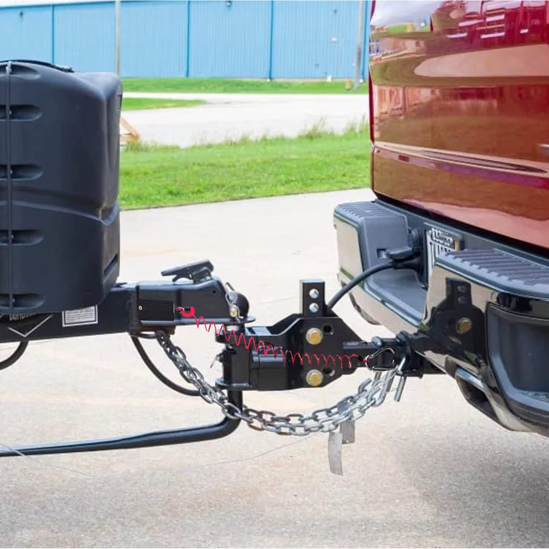 Red coiled breakaway lanyard running from a caravan A-frame breakaway switch to a weight distribution hitch on a red ute, with safety chains crossed underneath